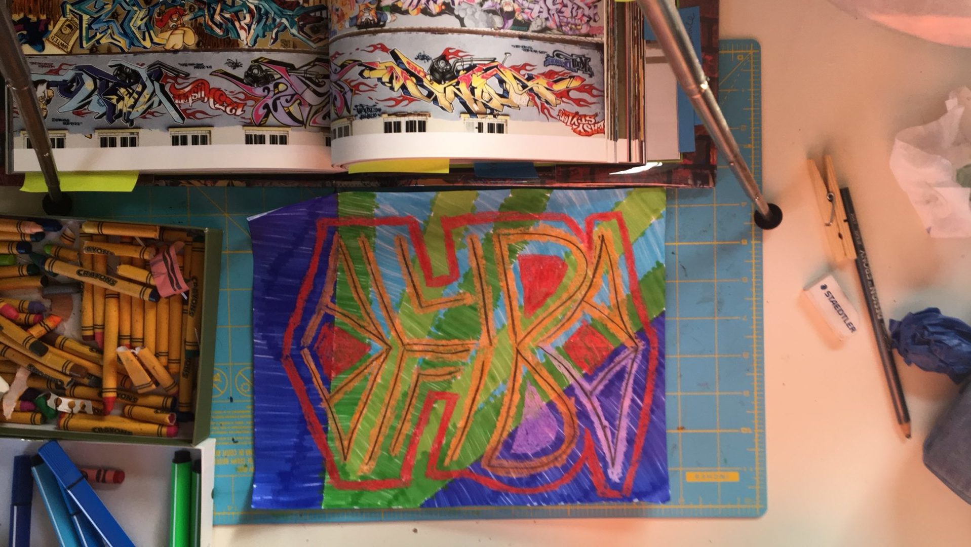 A colorful drawing with crayons and a book. The drawing is of my name both upside-down and right-side up.  